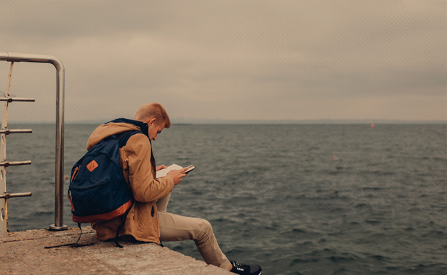 A man on a pier, uncertain about the book he is reading.