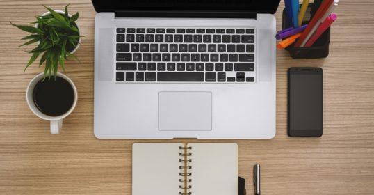 A laptop on a desk next to a notebook and a cup of coffee, creating the perfect work life setup.