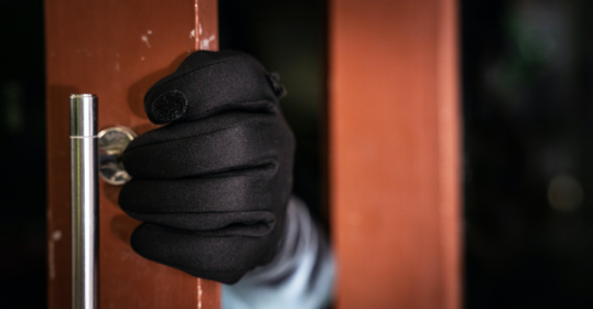 A person in a black glove is holding a door handle to prevent home invasion.