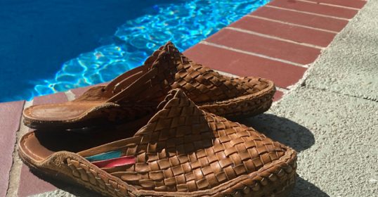 A pair of brown woven slippers by the pool during summertime.