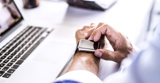 A man is using a smartwatch while working on a laptop.