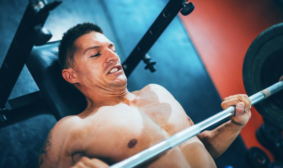 A man bench pressing a barbell with a spotter in the gym.