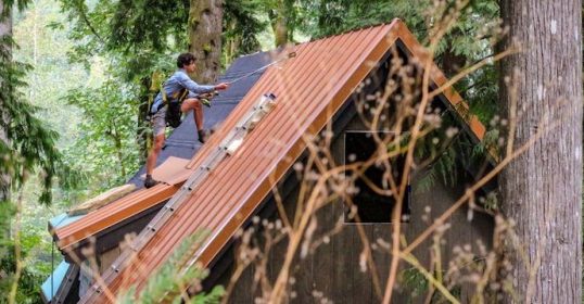 man on roof of cabin in the woods