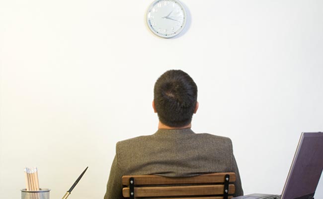 A man at a desk, gazing at a clock, is a prime example of procrastination and its effects on behavior.