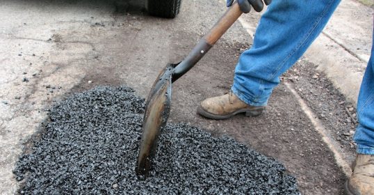 A man using a shovel to dig a hole in the road for maintenance.