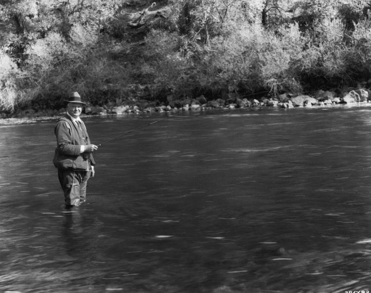 A man standing in a river with a fly rod enjoying some self-care.