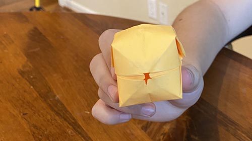 A person showcasing a yellow origami bird on a table.
