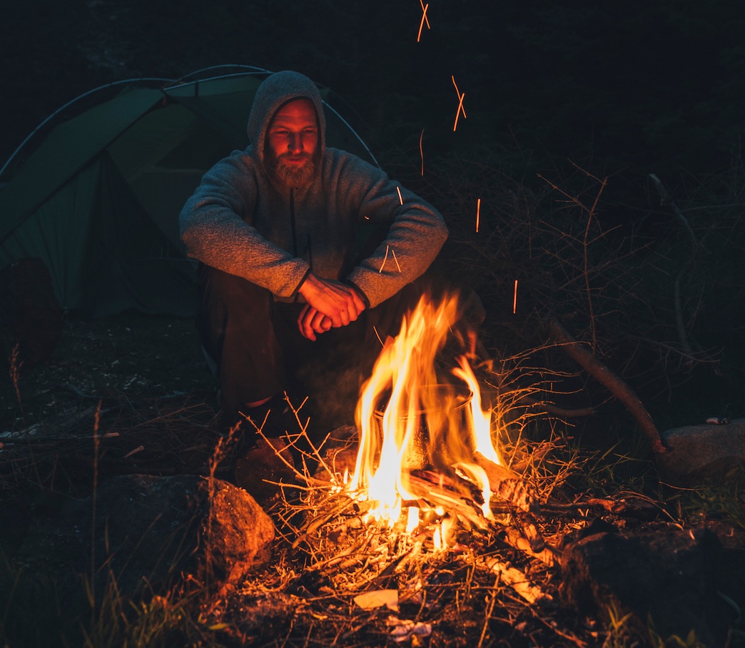 A man reflecting by a campfire.