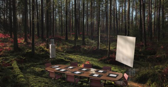 A table is set up in a forest with a projection screen for a podcast recording.