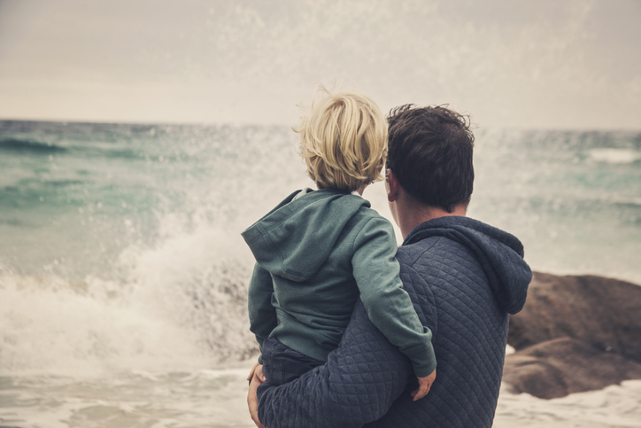 A man is holding a child while gazing at the ocean.