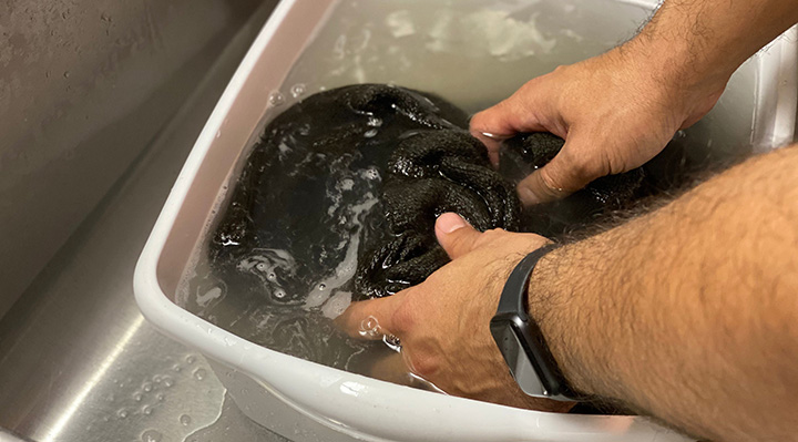 A person washing a black towel in a sink.