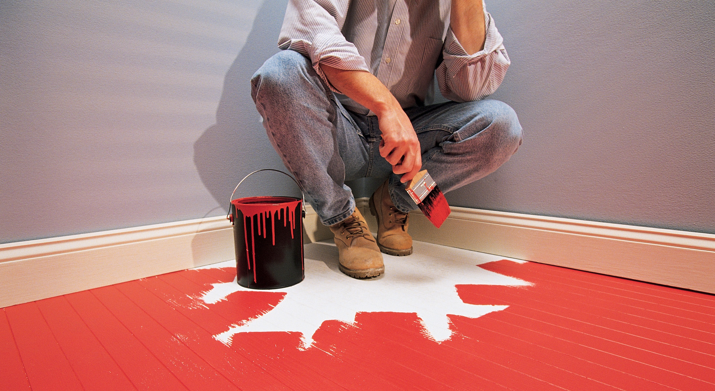 A man painting a room with red paint while listening to a podcast.