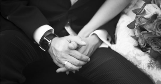 A perfect black and white photo of a bride and groom holding hands.