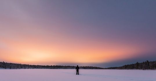 A person showcasing Sisu stands on a snow covered field at sunset.