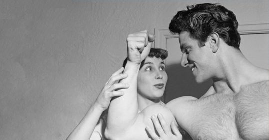 A black and white photo of a man and woman flexing their muscles.