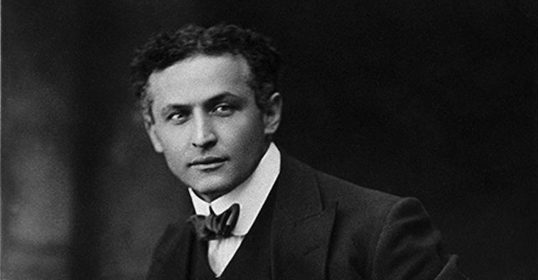 A vintage photo of a man in a suit with a mysterious aura, reminiscent of Harry Houdini.
