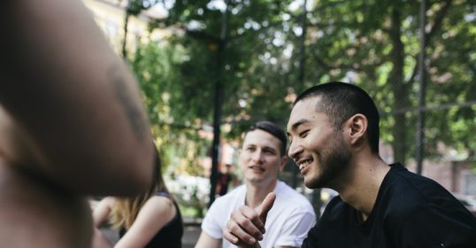A group of people sitting on the ground in a park, engaging in an episode of their podcast.