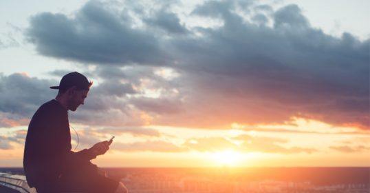 A man sitting on a ledge, quietly observing the sunset.