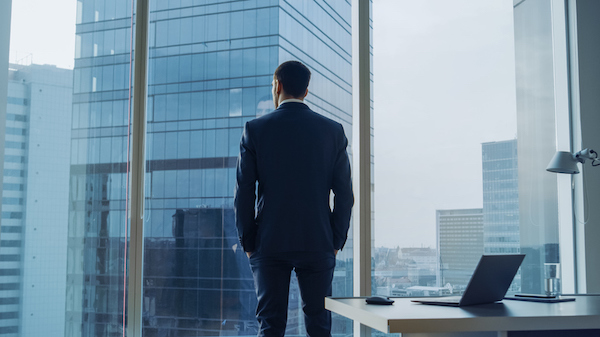 A businessman in a suit standing in front of a window, wanting to record a podcast.