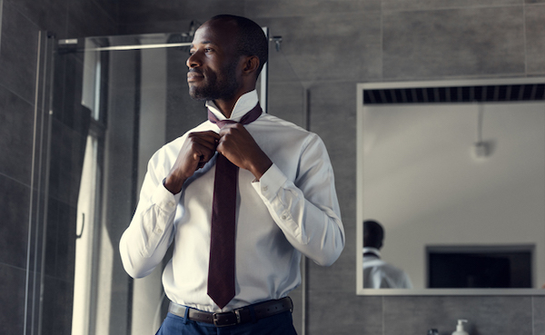 A man is adjusting his necktie in a bathroom.