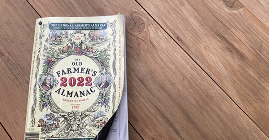 An old Farmer's Almanac rests on a wooden floor, praised for its wisdom.