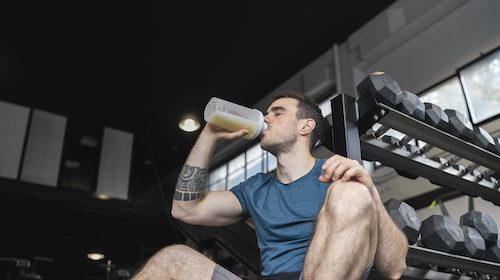A man drinking a green protein shake in a gym.