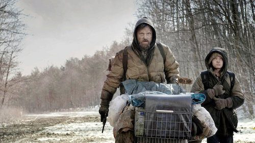 A couple braving a snowy journey with bags on their backs, reminiscent of Cormac McCarthy's 