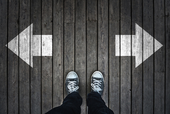 A person standing on a wooden floor with two arrows pointing in different directions, trying to make a big decision.