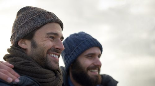 Two men with beards and hats smiling while making friends.
