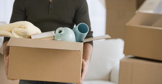 A man holding a box of boxes in his living room, looking to downsize and declutter.