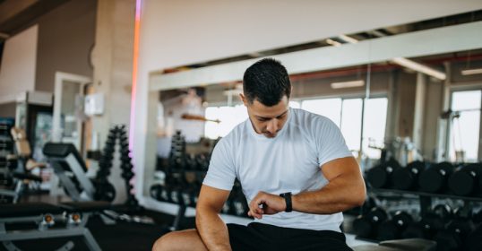 A man resting on a bench in the gym after completing his weightlifting sets.
