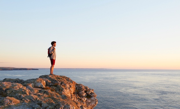 A man looking out at the ocean from the cliff top.