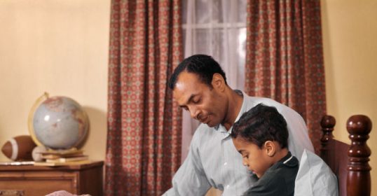 A father and son reading a book together in bed.