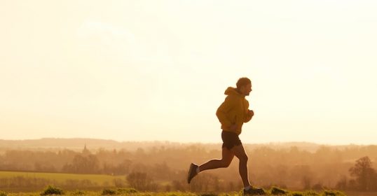 A person engaged in their fitness routine, running in a field at sunset.