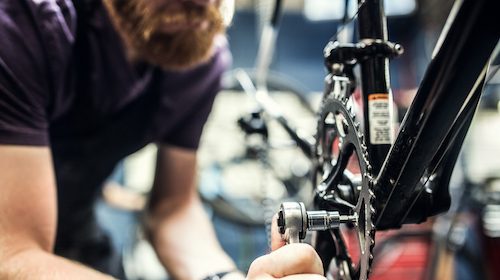 A man is conducting bike maintenance on a bicycle in a shop, possibly fixing an inner tube or applying a patch.