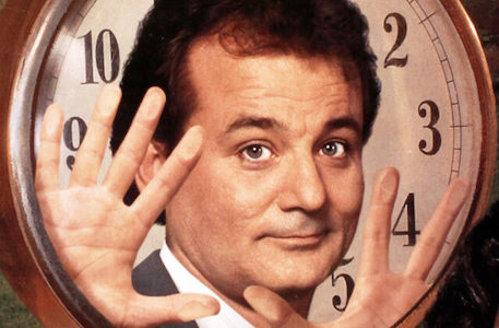 A man in a suit is holding his hands up in front of a clock, possibly reflecting on his Podcast or Groundhog Day.