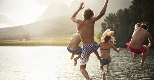 A group of people having fun jumping into a lake.