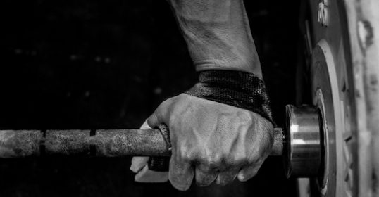 A black and white photo of a weightlifter's hand holding a barbell.