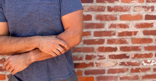A man in a blue shirt leans against a brick wall.