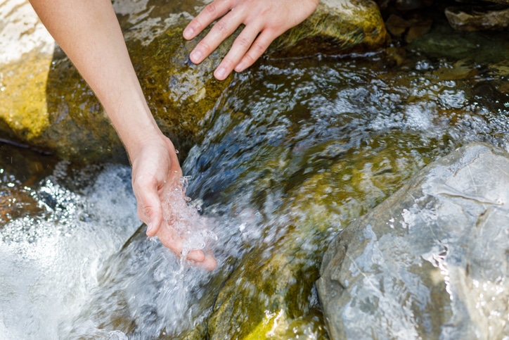 A woman is washing her hands in a stream of water with a sense of focus and efficiency.