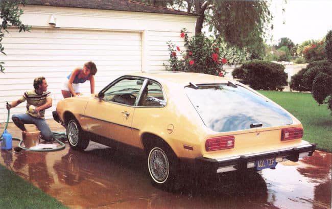 Two people protect a yellow car in a driveway.