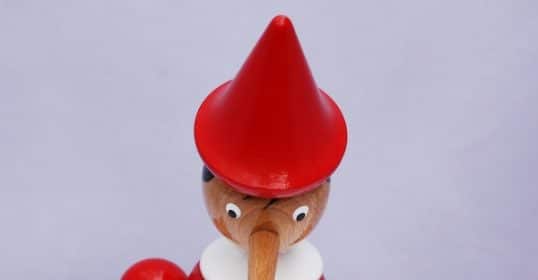 A wooden elf with a red hat is standing on a white piece of paper.