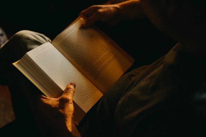 Person reading a book on the importance of cultural literacy in dim lighting.