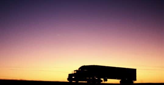 Silhouette of a truck driving at dusk against a gradient sky, embodying the spirit of 
