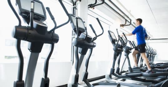 Man exercising on an elliptical machine in a gym, focusing on Zone 2 Cardio.