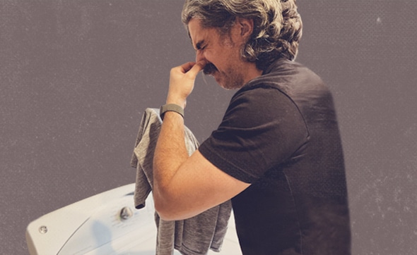 Man pinching the bridge of his nose in frustration or fatigue, overwhelmed by how to get the stink out of synthetic workout shirts.