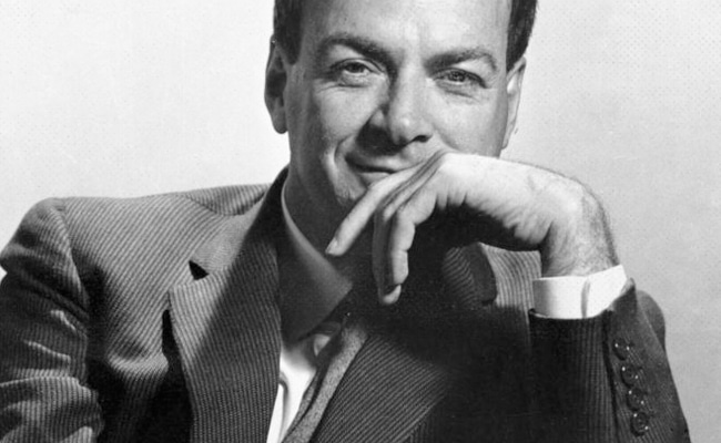 Black and white photo of a smiling man in a suit, resembling Richard Feynman, resting his chin on his hand.