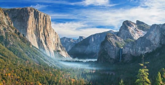 Scenic view of Yosemite Valley with El Capitan on the left, Half Dome in the distance, and a light mist above the forest floor in one of the most iconic National Parks.