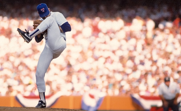 Baseball pitcher Nolan Ryan in mid-throw during a game with spectators in the background.