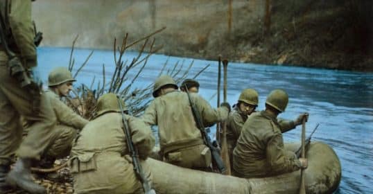 Soldiers in military uniforms using an inflatable raft to cross a river in one of the amazing WWII photos.